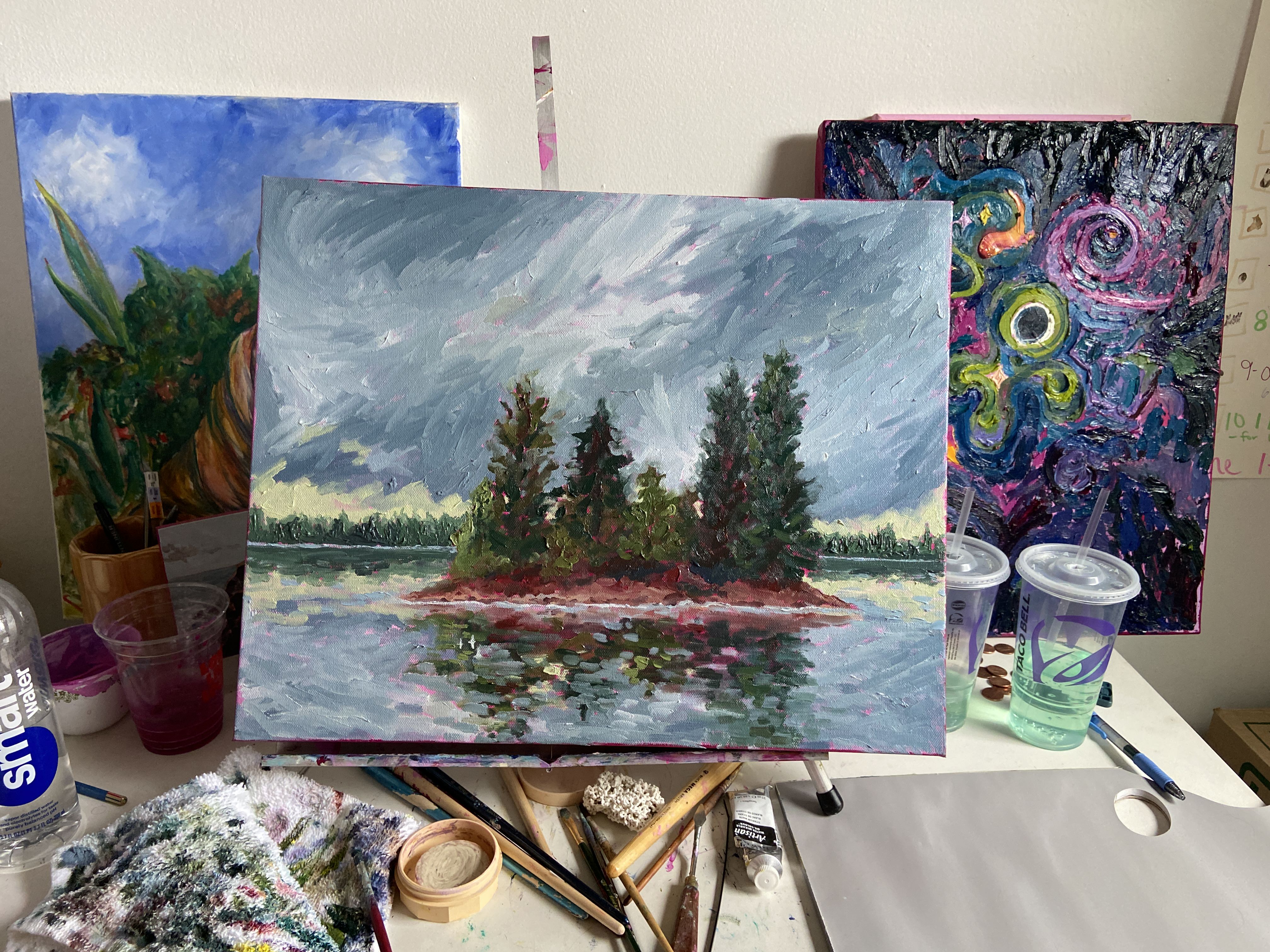 Signature Sunflower oil painting of an island in a bay with the stormy sky reflecting in the water. There are several trees on the small island in the center of the painting and the bay. It feels like a rainy PNW day.